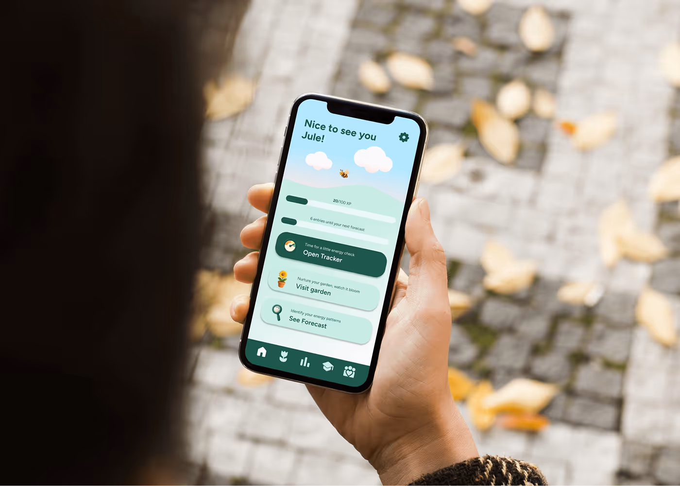 Hand holding smartphone displaying an app with greeting, weather info, and options like "Open tracker," "Visit garden," and "See forecast."