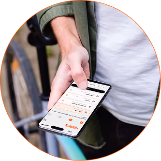 Hand holding a smartphone displaying redesigned barmer app dashboard with a bicycle wheel visible in the background.