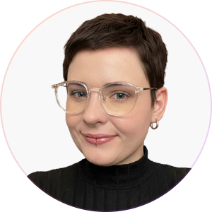 Person with short dark hair, clear eyeglasses, lip piercing, and small hoop earrings, wearing a black turtleneck.