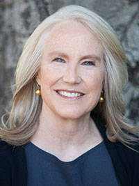 Smiling middle-aged woman with long silver hair wearing gold earrings and a dark top.