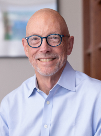 Smiling bald man with glasses wearing a light blue button-up shirt indoors.