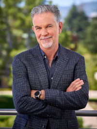Middle-aged man with gray hair wearing a dark blazer and watch, standing outdoors with arms crossed.