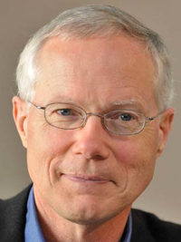 Portrait of an older man with white hair, glasses, and a slight smile wearing a black jacket.