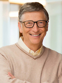 Smiling man with glasses wearing a beige sweater over a light shirt in a softly lit room.