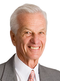 Smiling elderly man in a suit and tie with white hair against a white background.