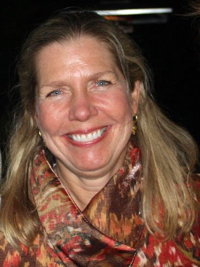 Smiling woman with long blond hair wearing a multicolored patterned scarf and gold earrings.
