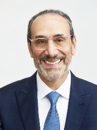 Smiling middle-aged man with glasses, beard, and suit with blue tie on a white background.