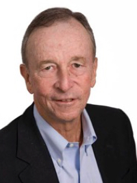 Portrait of an older man in a black blazer and light blue shirt against a white background.