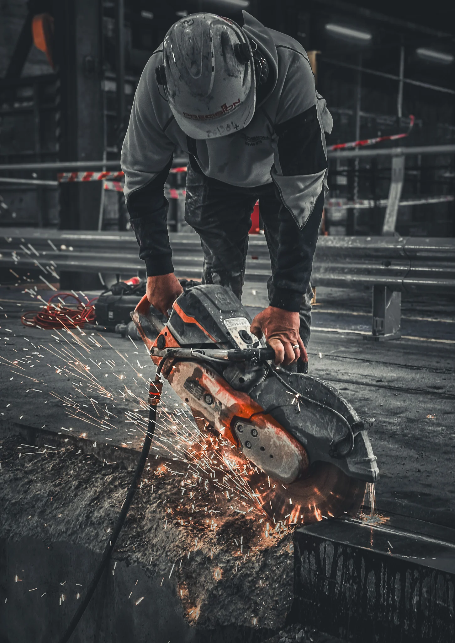 Construction worker wearing a helmet using a power saw to cut concrete, creating sparks.