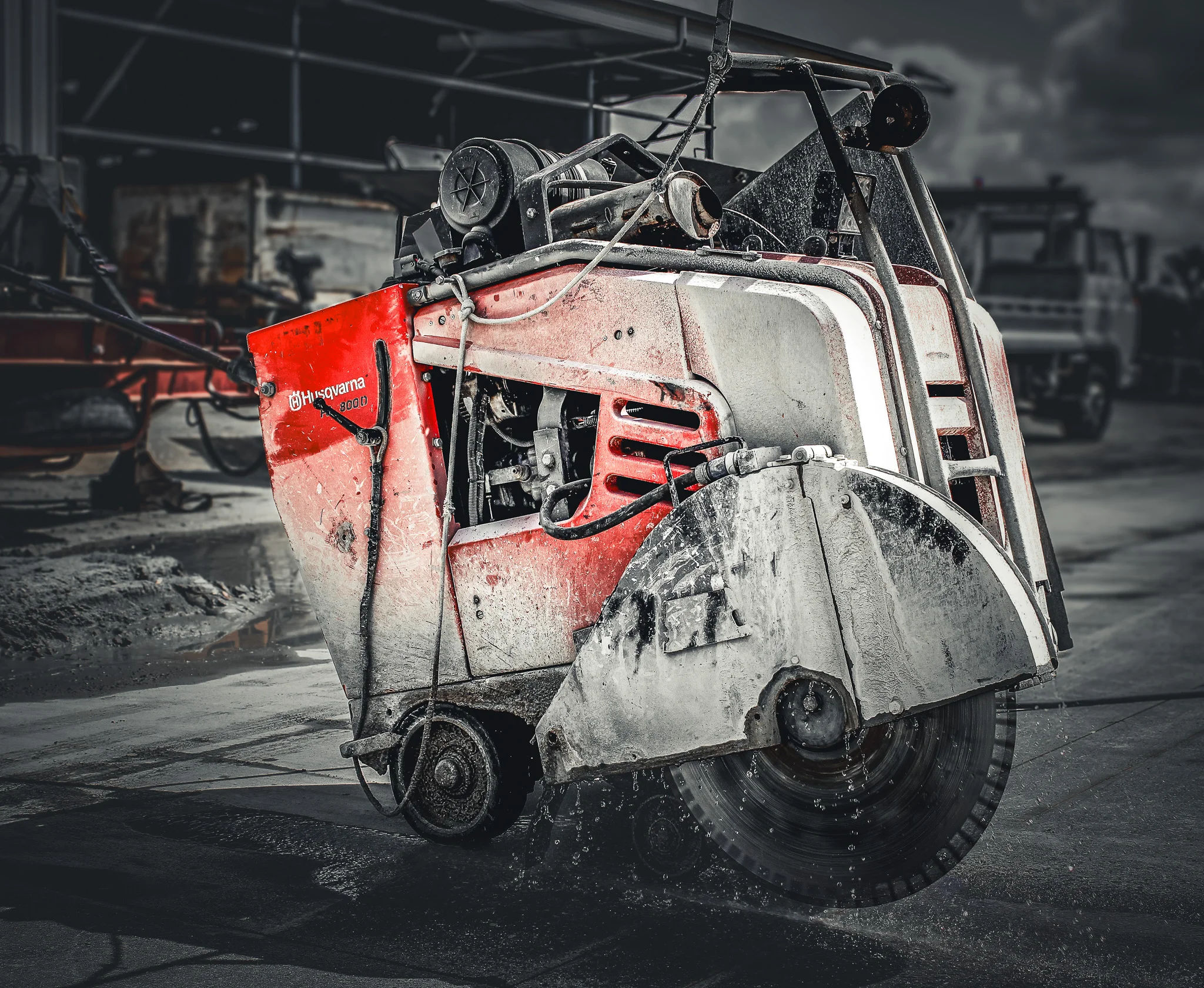 Red and white Husqvarna concrete saw with water spraying on the spinning blade at a construction site.