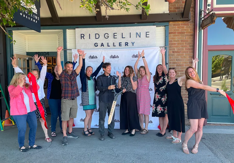 Group of ten people celebrating a grand opening outside Ridgeline Gallery with a ribbon-cutting ceremony and oversized scissors.