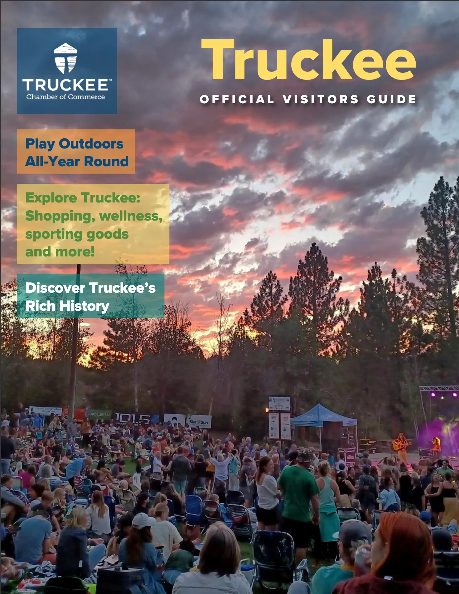 Crowd gathered outdoors at sunset watching a live music performance in a forested area with tall pine trees.