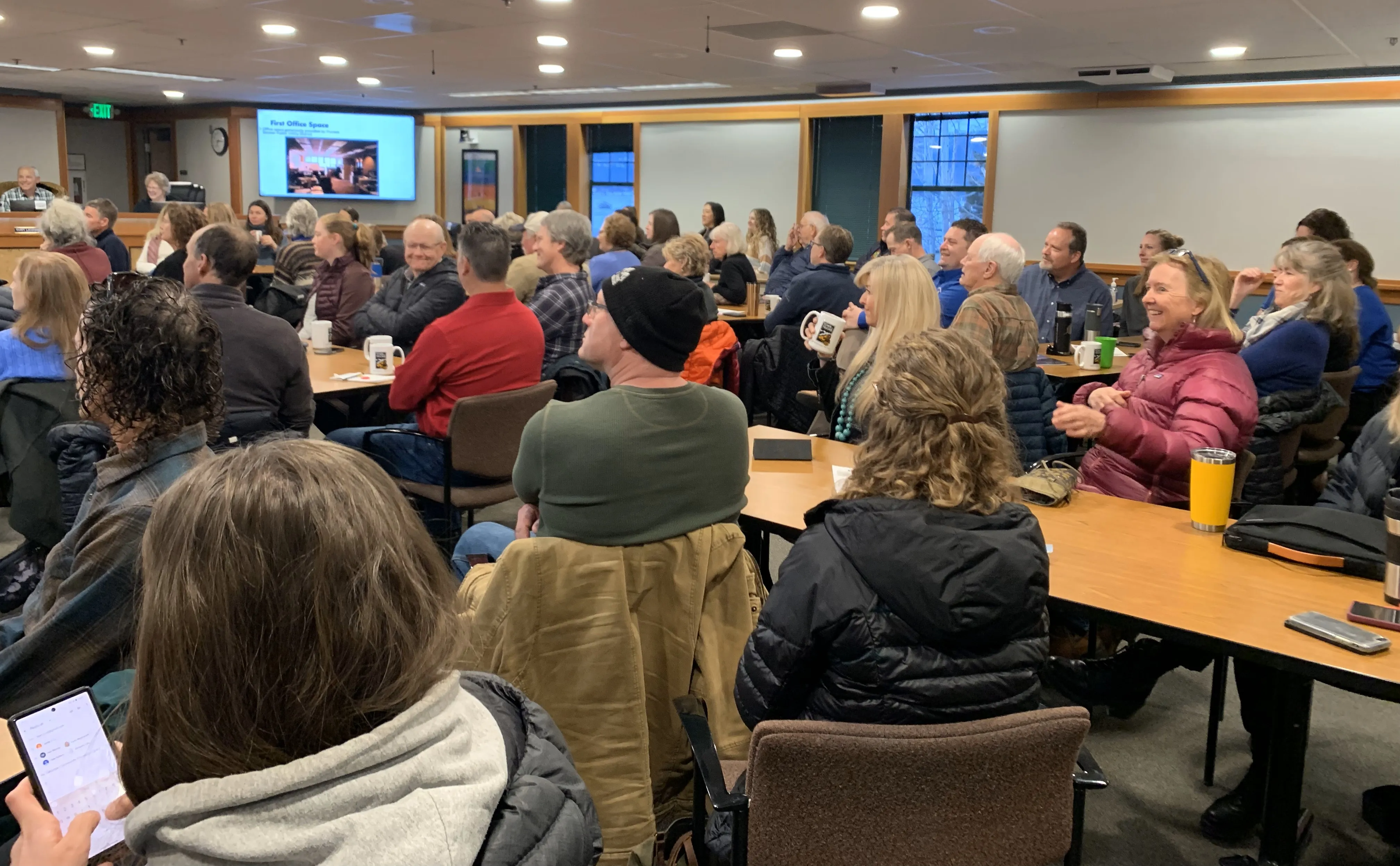 A group of adults seated at tables in a conference room attentively watching a presentation.