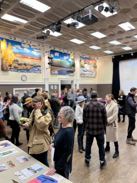 People socializing inside a community center with colorful landscape paintings on the walls.