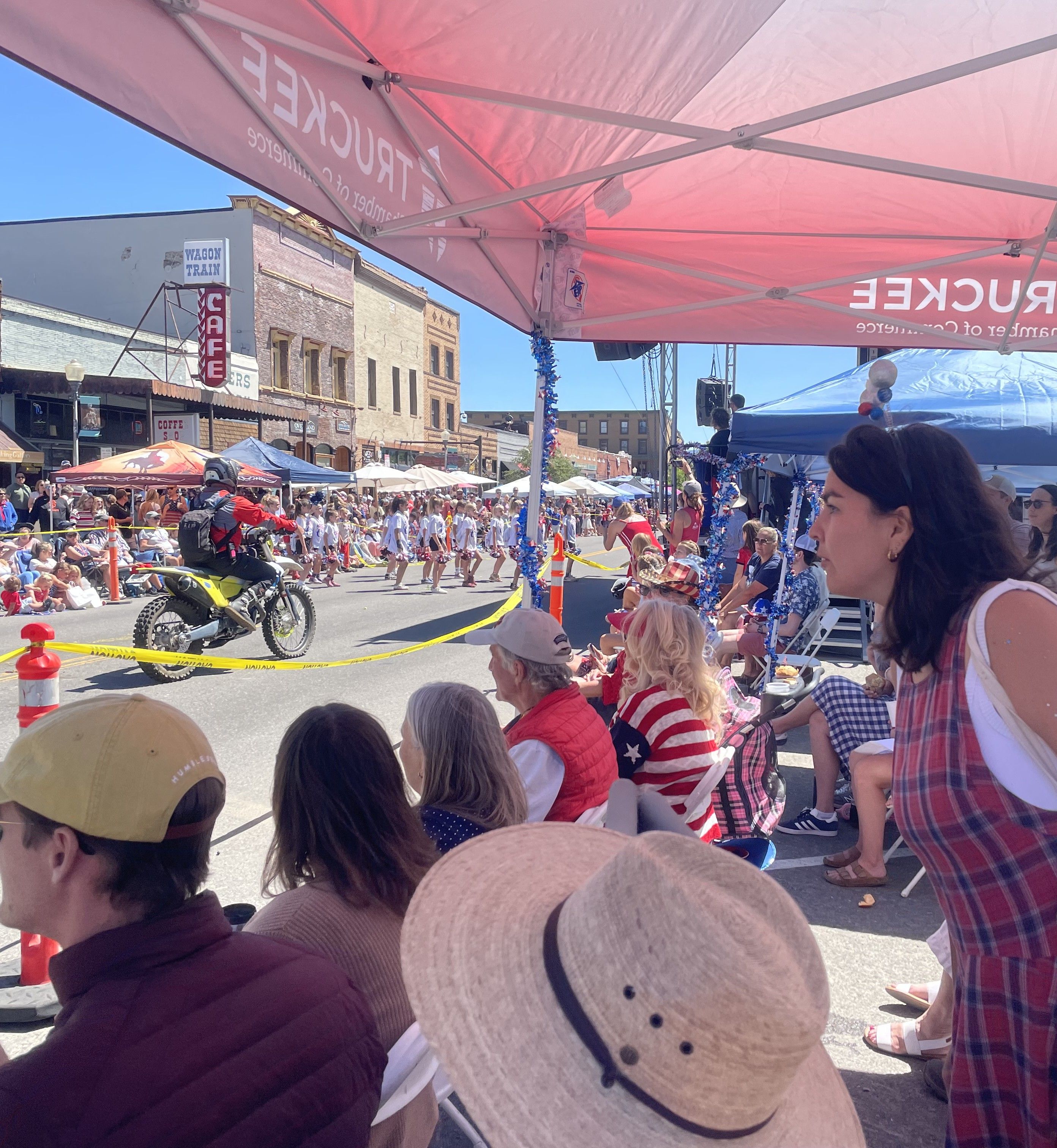 Two female police officers and a bulldog wearing a patriotic hat sitting on the back of a pickup truck during a street parade.