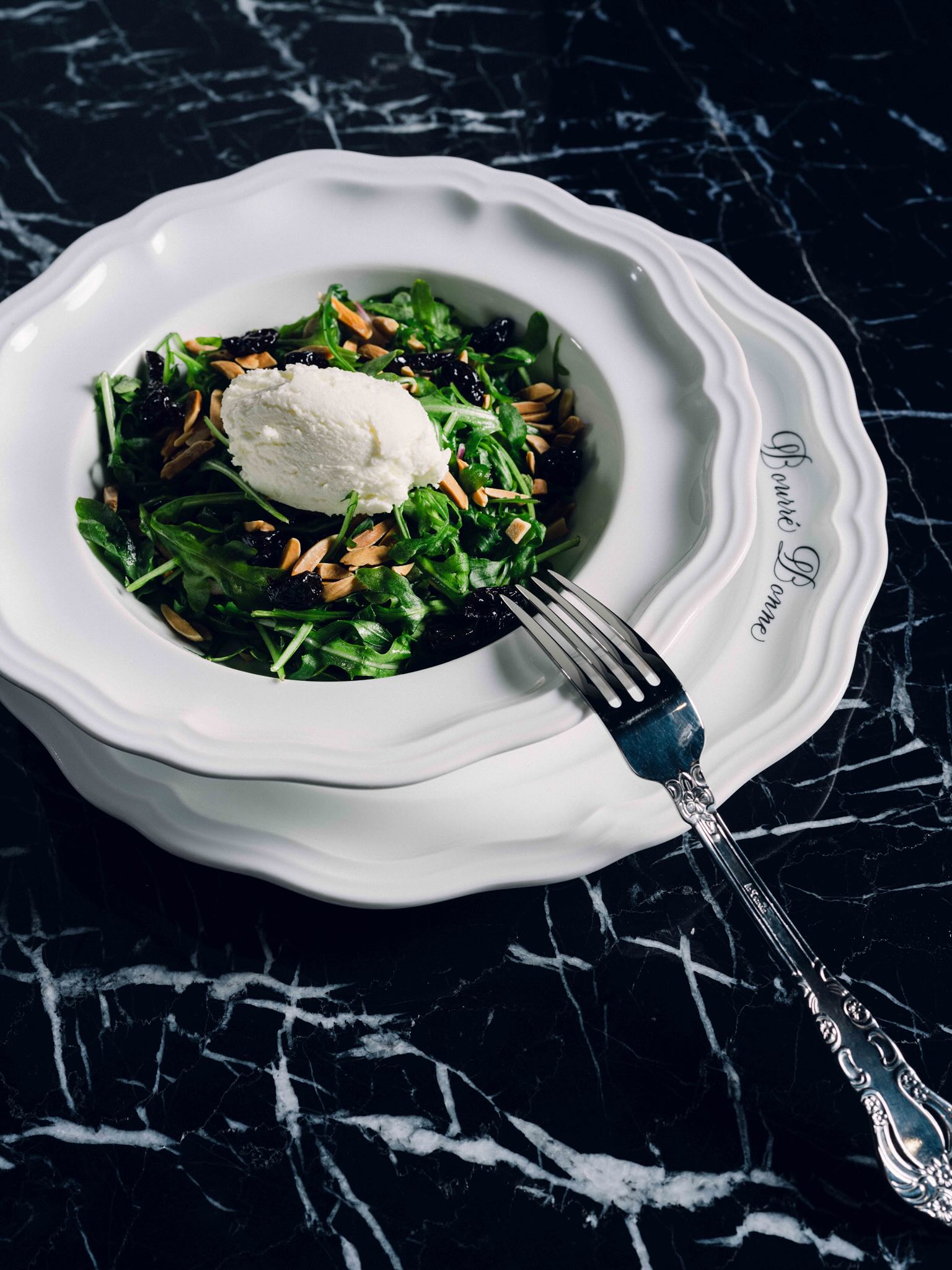 A white bowl filled with a salad and a fork.