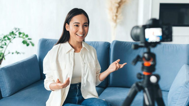 Smiling woman recording video content on camera while sitting on blue couch