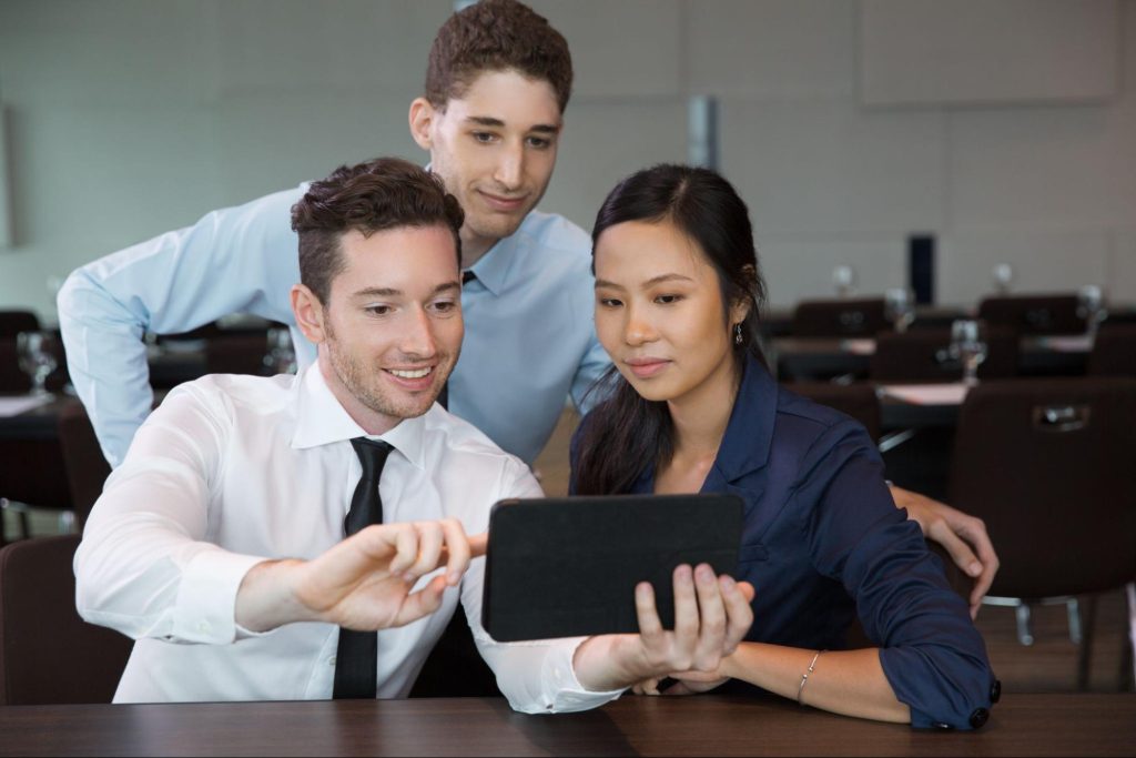 Three business professionals collaborating and reviewing content on a tablet in modern office