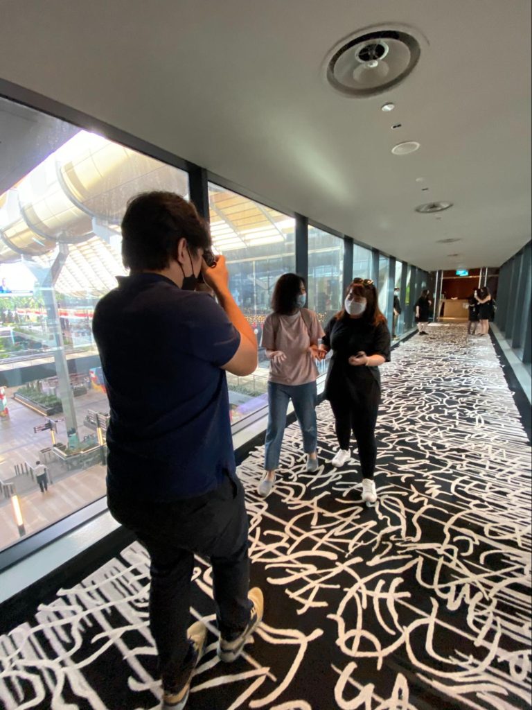 Person taking photo in modern hallway with patterned carpet and large windows overlooking cityscape