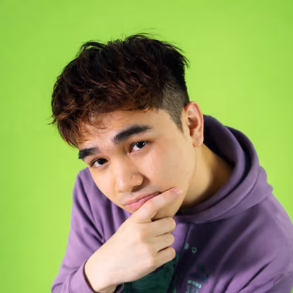Young man in purple hoodie with hand on chin against bright green background