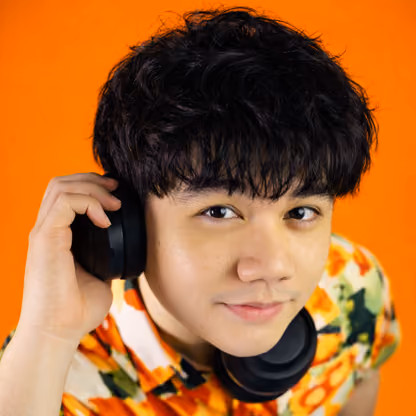 Young person with black short hair wearing colorful jacket against orange background.