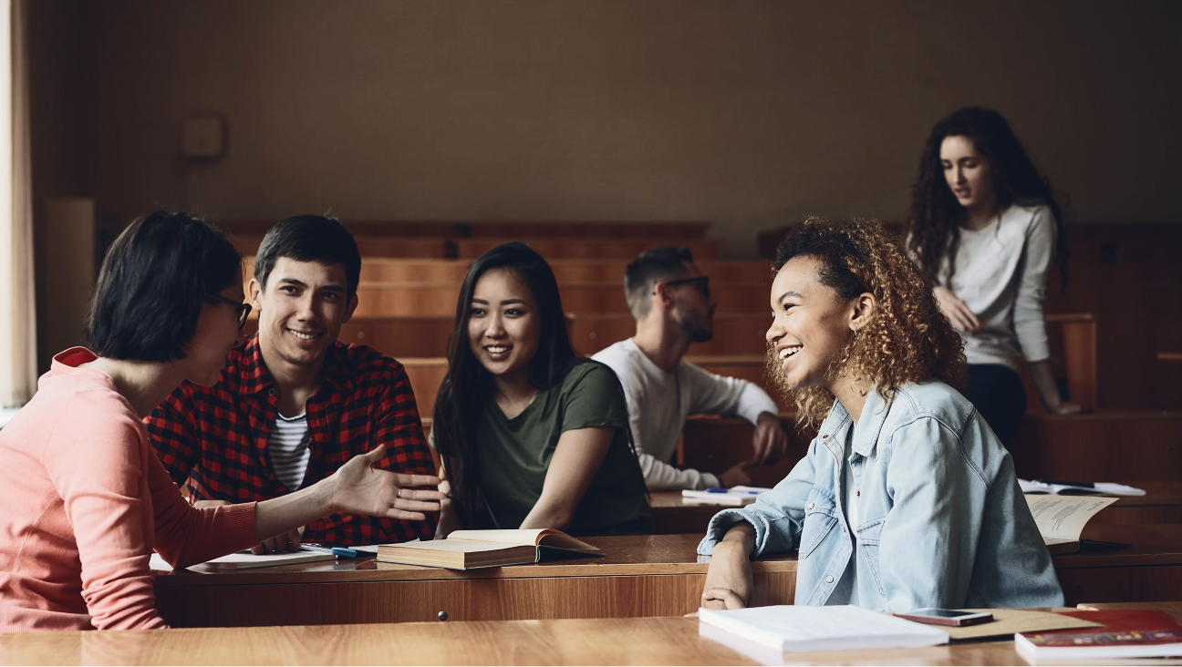 Group of diverse students engaged in discussion in a wooden classroom or library setting.
