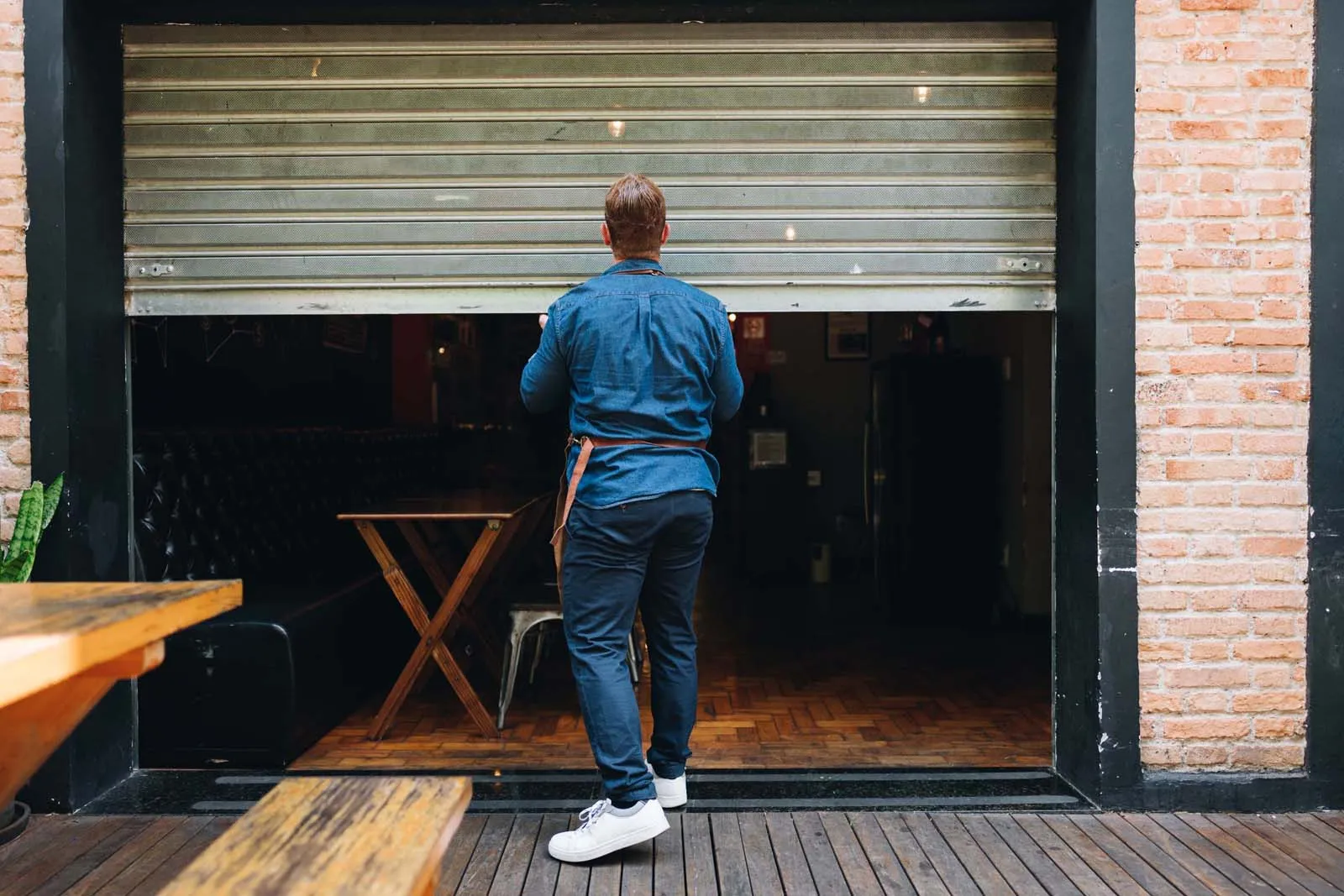 Man opening a café by lifting a metal shutter door in the morning.