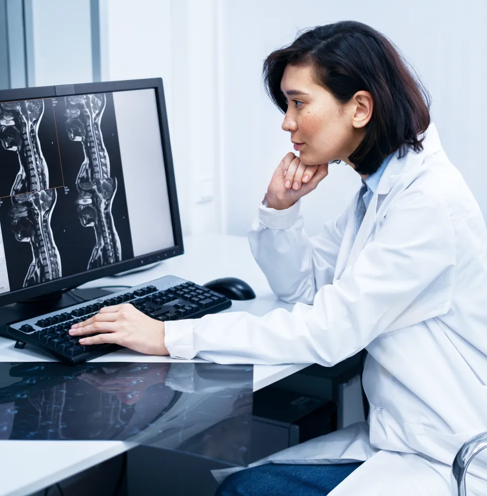Female doctor in a white coat analyzing spinal MRI scans on a computer monitor.