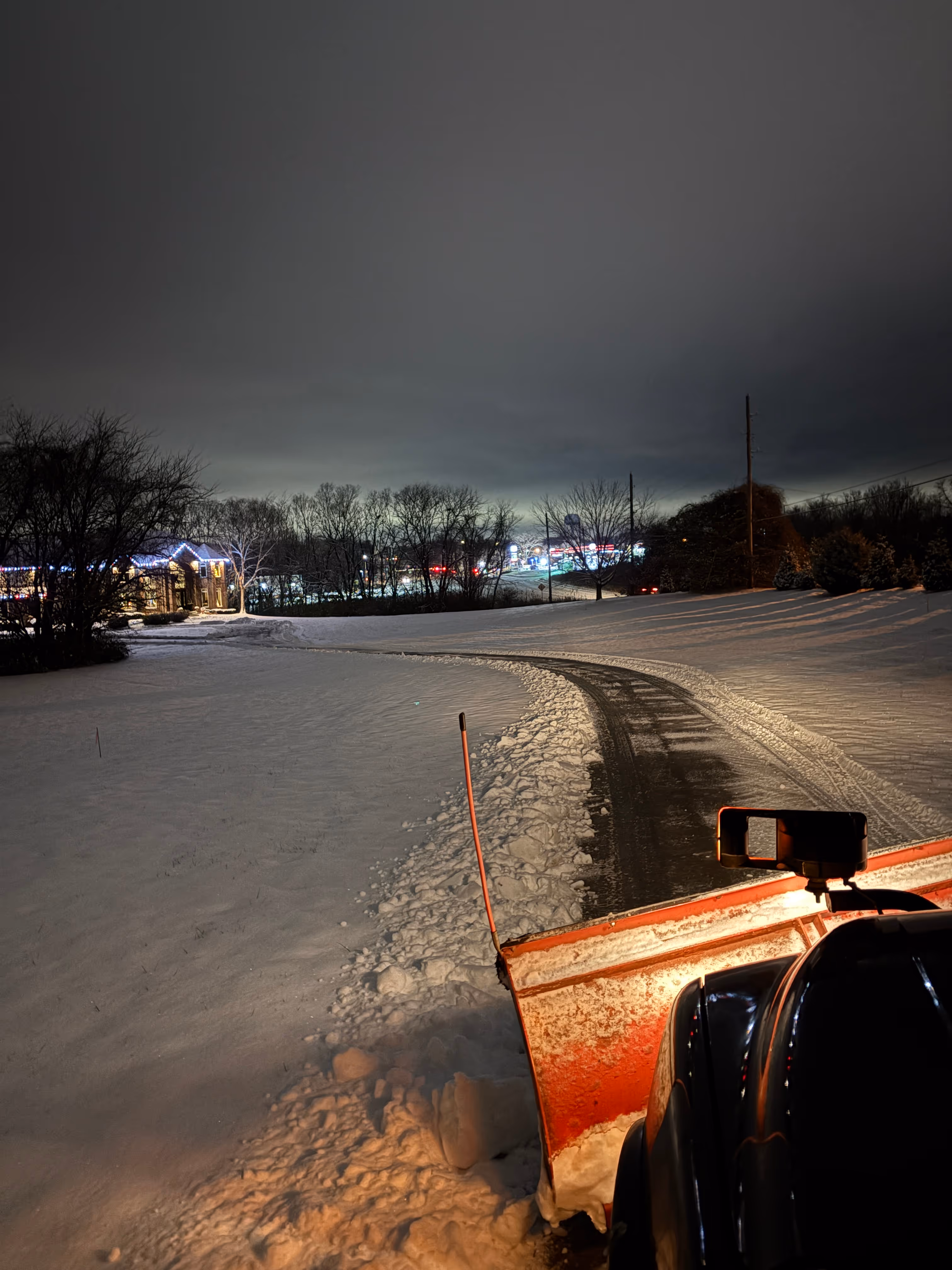 Snow plow clearing a residential driveway at night during a winter storm, serviced by Marrs Lawn and Landscape in Grain Valley, MO.