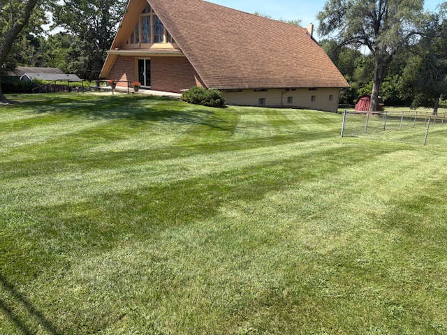Thick green lawn with mowing stripes next to a residential home, maintained with fertilization service by Marrs Lawn and Landscape in Grain Valley, MO.