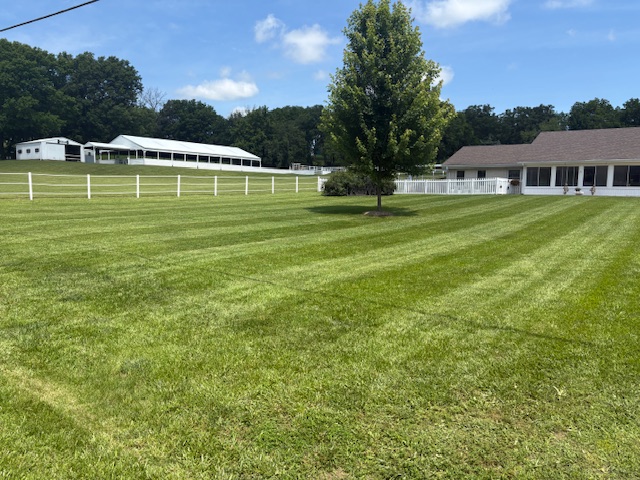 Large residential property with lush mowed lawn, white fence, and barn serviced by Marrs Lawn and Landscape in Missouri.