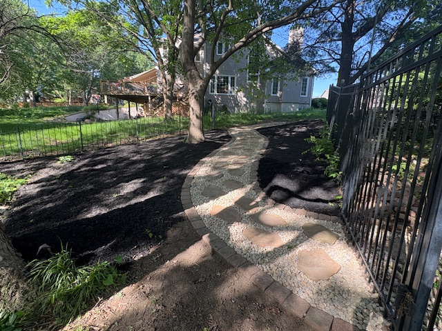 Shaded stone pathway with iron fence and mulched landscape beds, serviced by Marrs Lawn and Landscape in Missouri.