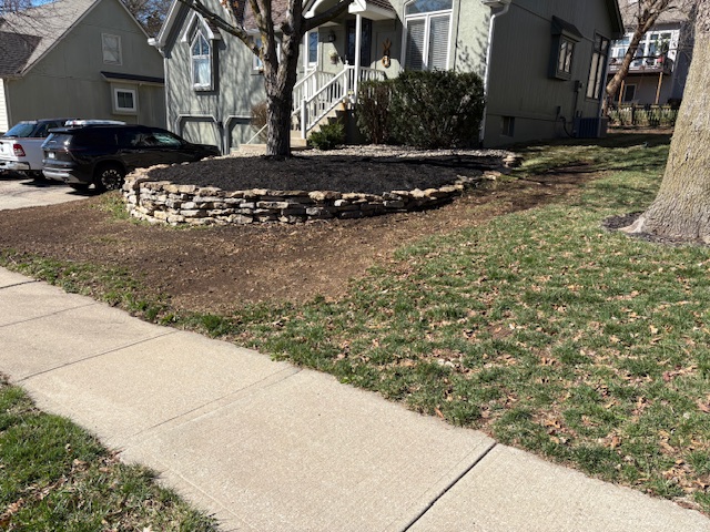 Stone retaining wall and freshly mulched landscape bed installed by Marrs Lawn and Landscape in Grain Valley, MO.