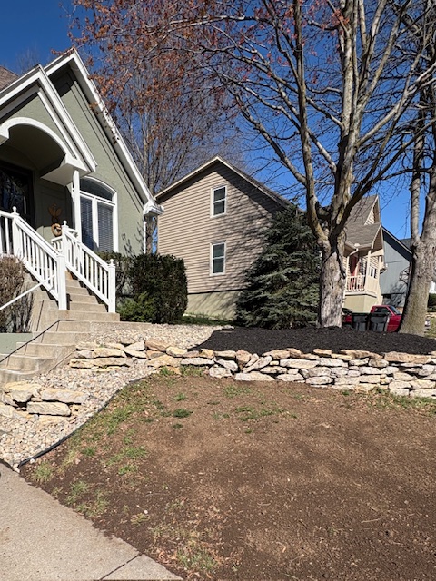 Stone retaining wall with freshly mulched landscape bed along front porch steps, installed by Marrs Lawn and Landscape in Grain Valley, MO.