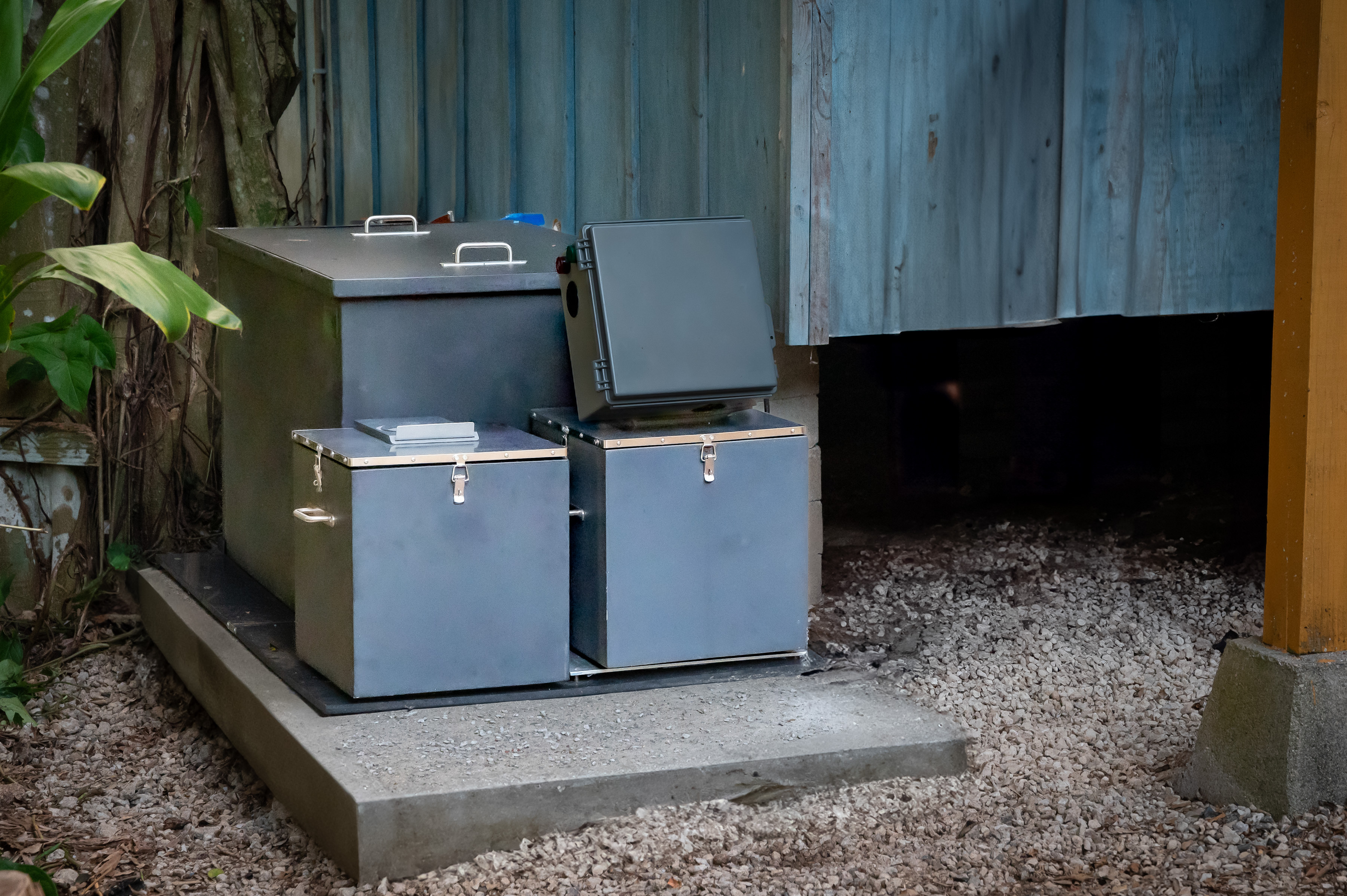 Mata Solid Waste Interceptor, Installed next to a home on a small concrete pad. Mata is a steel blue/grey color. 