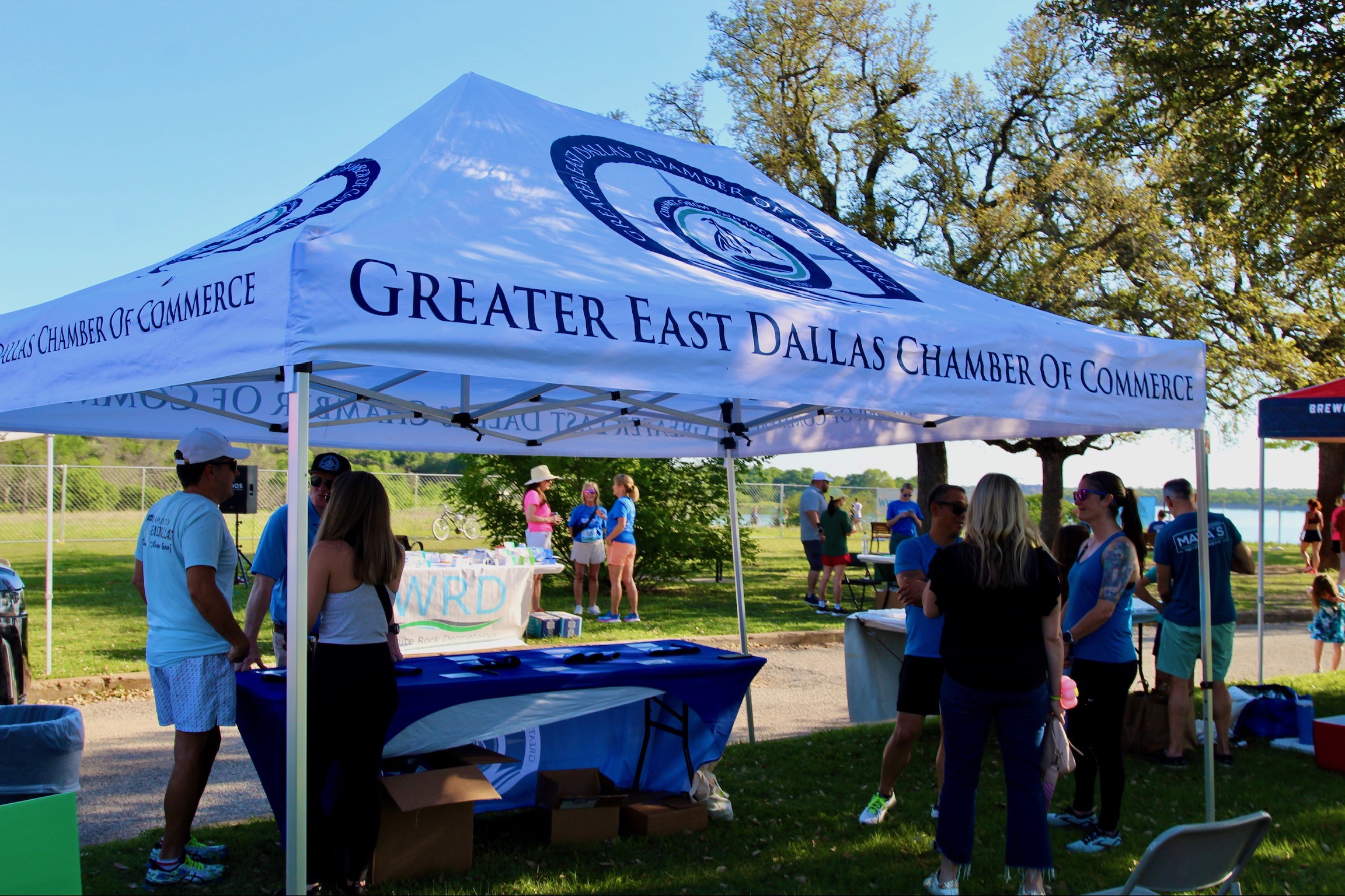 People gathered under a white tent with Greater East Dallas Chamber of Commerce at White Rock Lake in Dallas