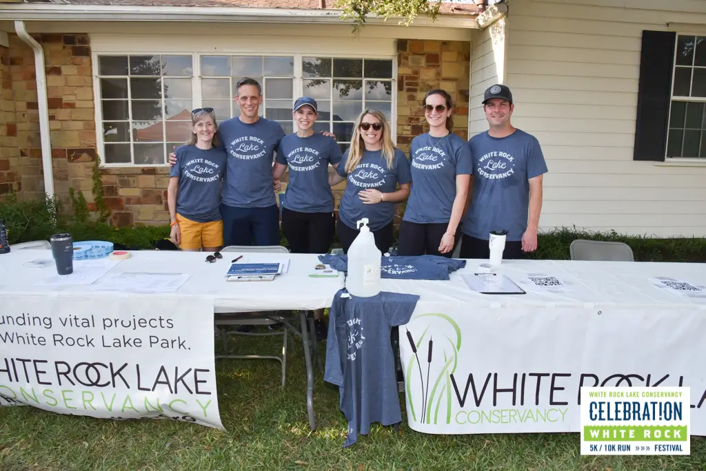 Six volunteers and members standing behind a table at the White Rock Lake Conservancy's Celebration White Rock