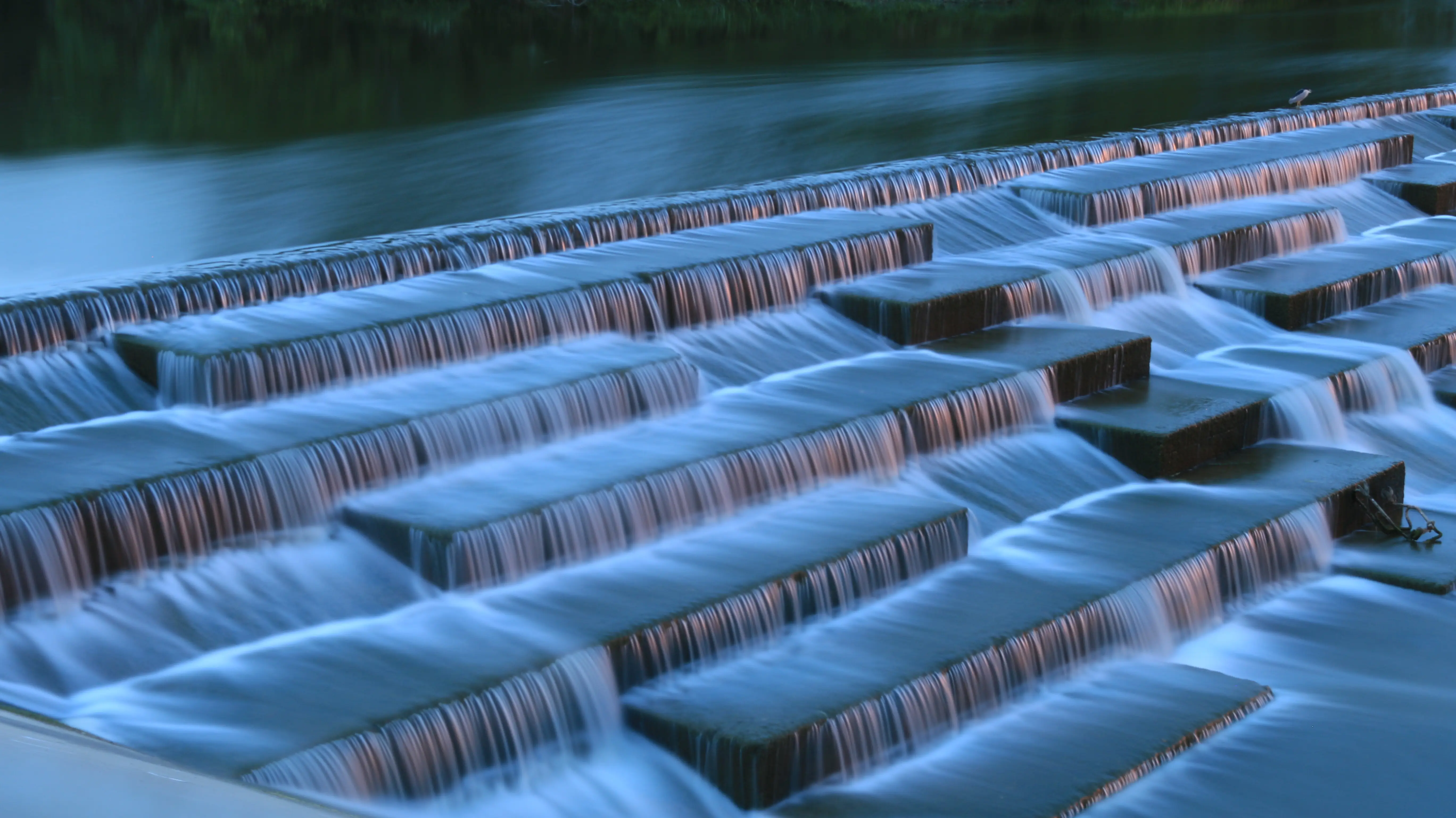 Multiple stepped concrete platforms creating a cascading spillway with smooth flowing water.