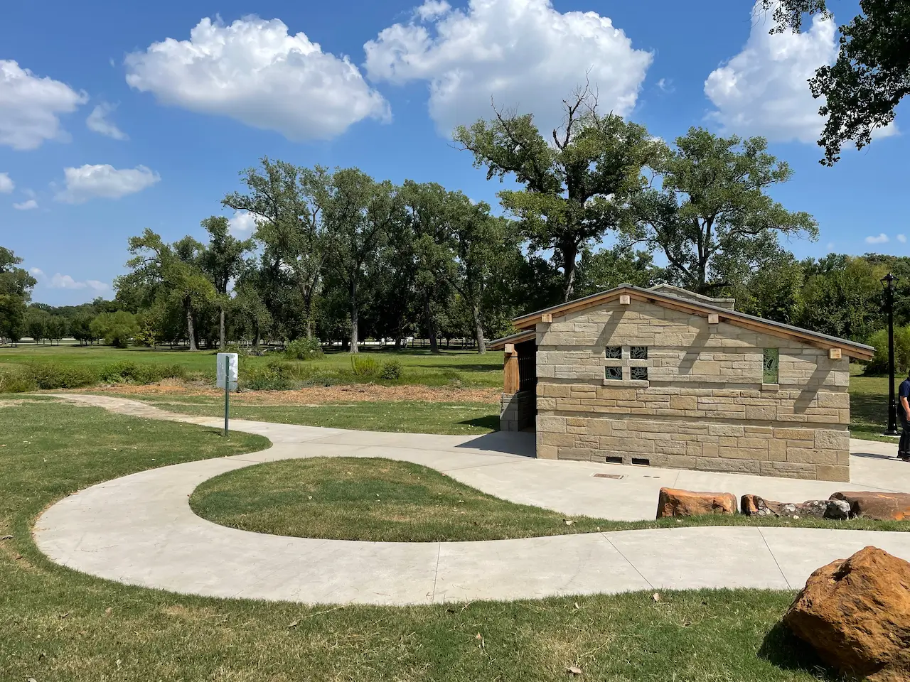 Stone restroom restoration at White Rock Lake Park in Dallas with small windows in a green park under a blue sky with clouds.