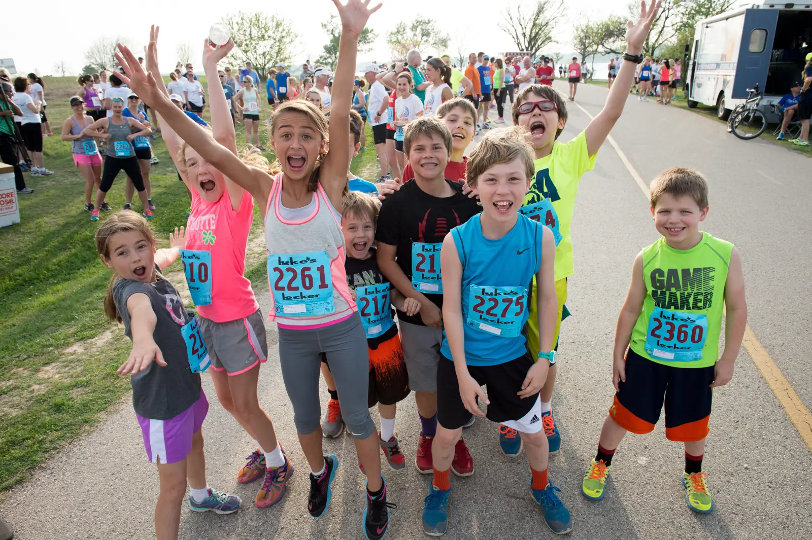 Group of energetic children wearing race bibs posing excitedly at Celebration White Rock race in Dallas, TX.