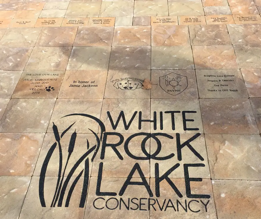Paved stone tiles with the logo and name White Rock Lake Conservancy and several engraved commemorative messages and images.