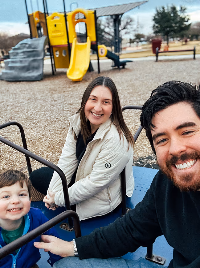 Jesse and his family sitting on playground equipment with a yellow slide and climbing structure in the background.