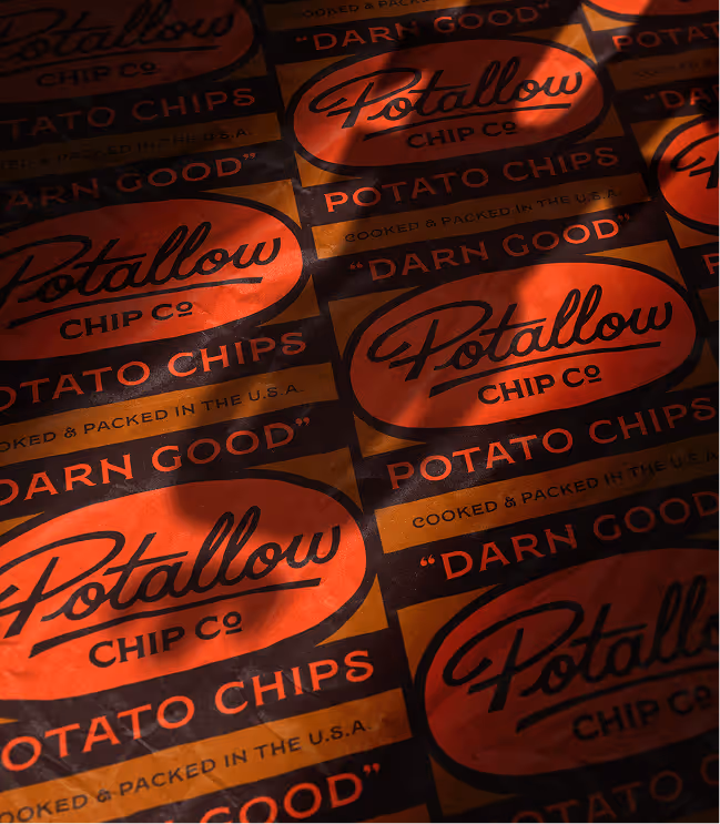 Multiple bags of Potallow Chip Co potato chips with orange and black packaging, featuring the slogan 'Darn Good'.