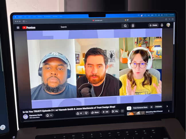 Laptop screen showing a YouTube video call with three participants, two men and one woman wearing headphones.