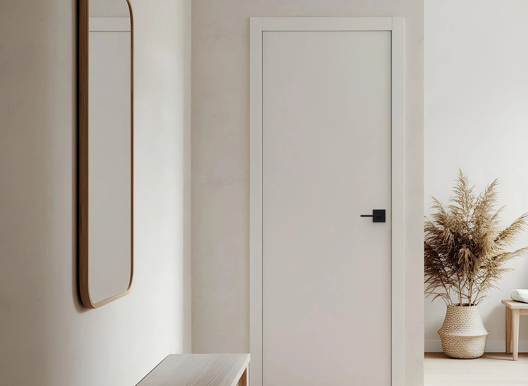 Minimalist interior featuring a closed light-colored door with a black handle, a tall wooden-framed mirror on the left wall, and a woven basket with dried plants on the right.