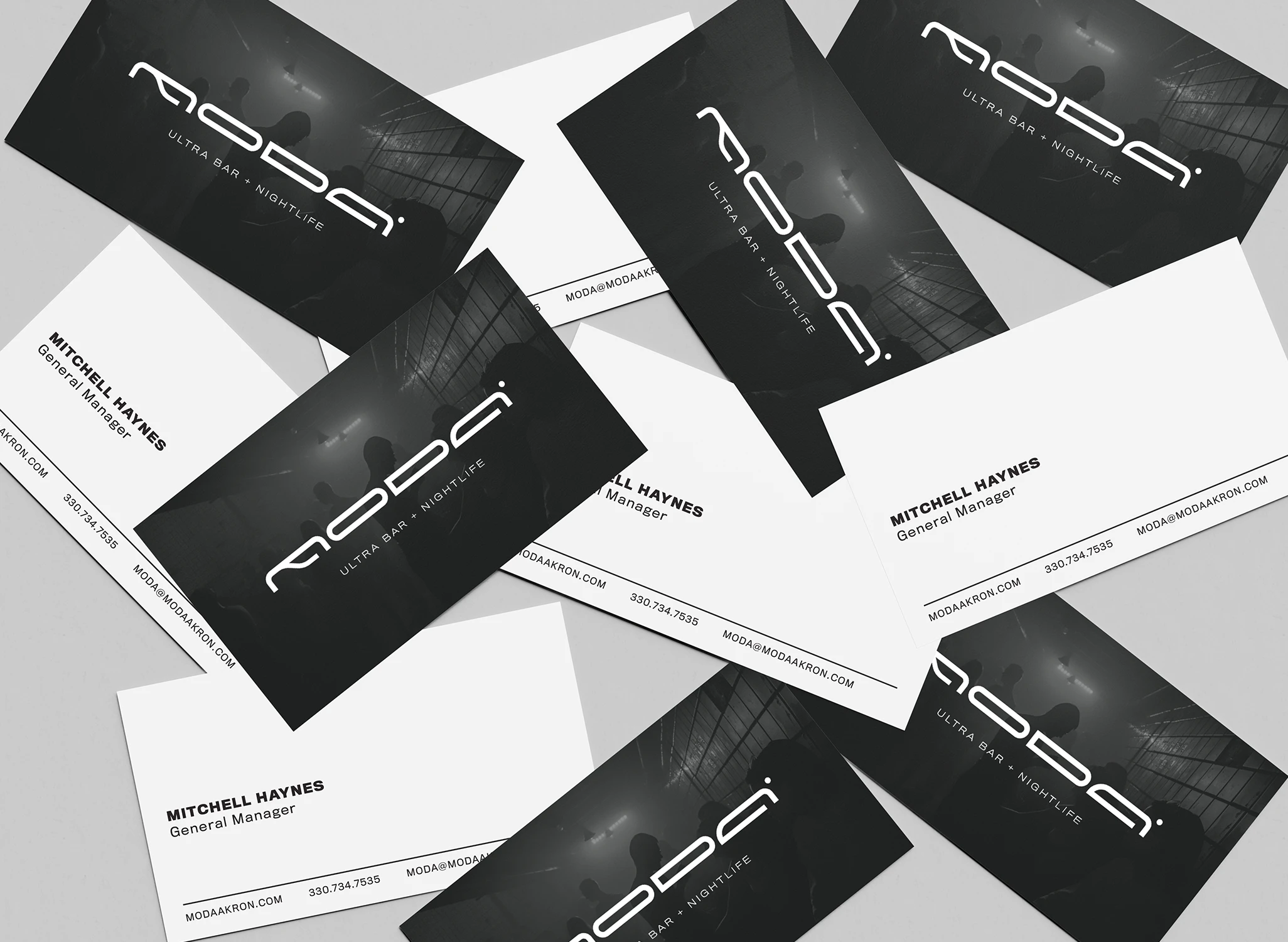 Scattered business cards with the MODA Ultra Bar and Nightlife logo depicted on one side in white on a dark background. The other side of the card is white with a generic "General Manager" contact listed.