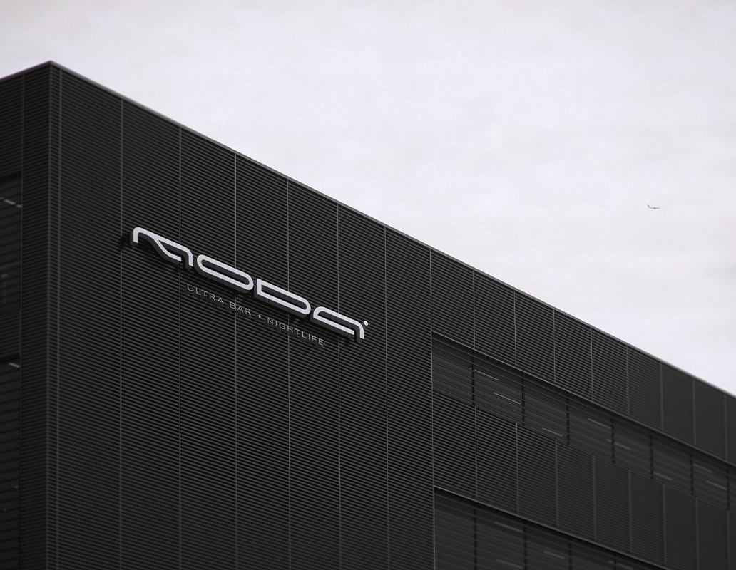 Modern industrial building facade with horizontal black slats and a sign reading 'MODA ULTRA BAR + NIGHTLIFE' against an overcast sky.