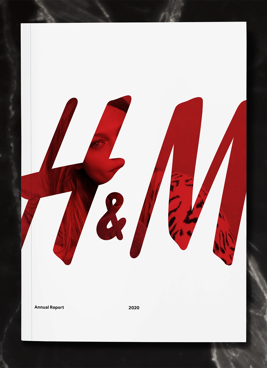 On black granite, a white booklet cover of H&M 2020 annual report with large red H&M logo partially showing a woman in the red of the logo wearing a leopard print shirt.