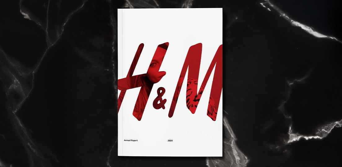 On black granite, a white booklet cover of H&M 2020 annual report with large red H&M logo partially showing a woman in the red of the logo wearing a leopard print shirt.