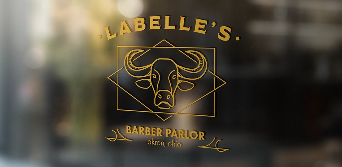 Gold lettering on glass showing 'LABELLE'S BARBER PARLOR akron, ohio' with a stylized buffalo head logo.